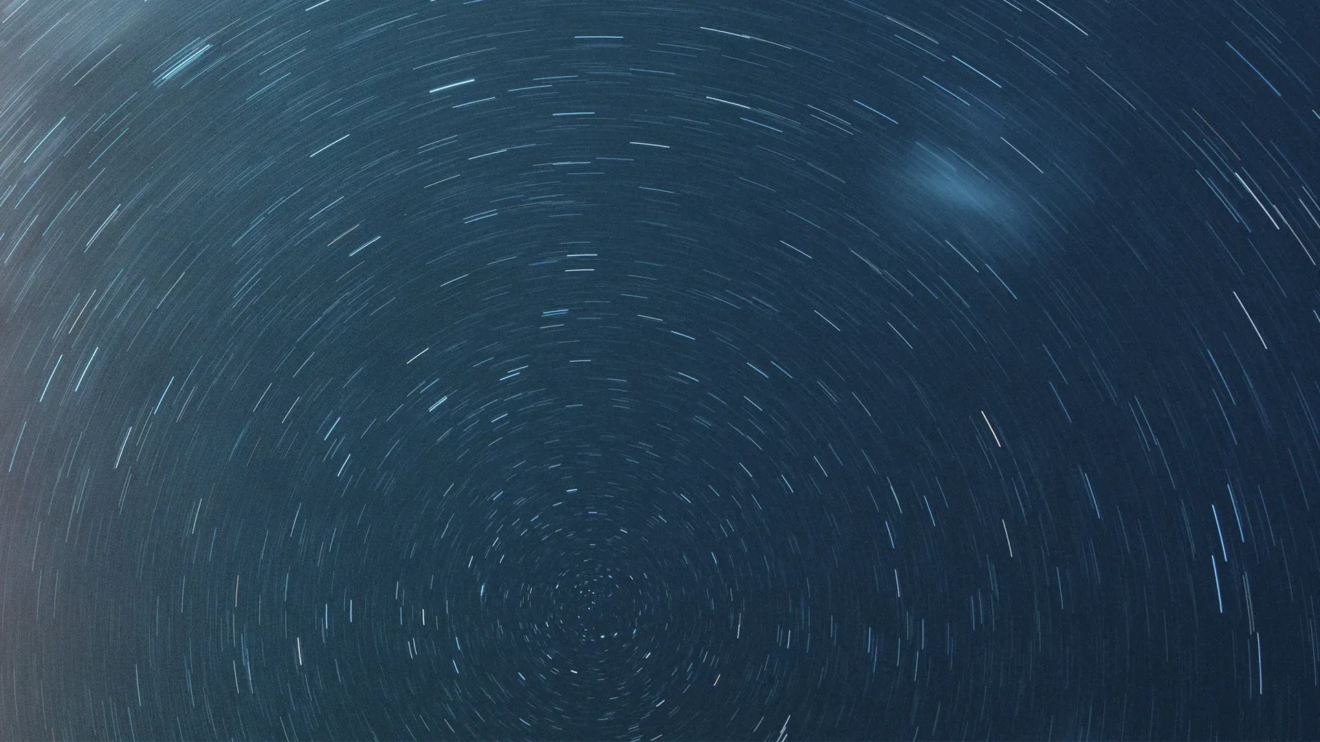 Night sky time-lapse showing stars in circular trails against a deep blue background.