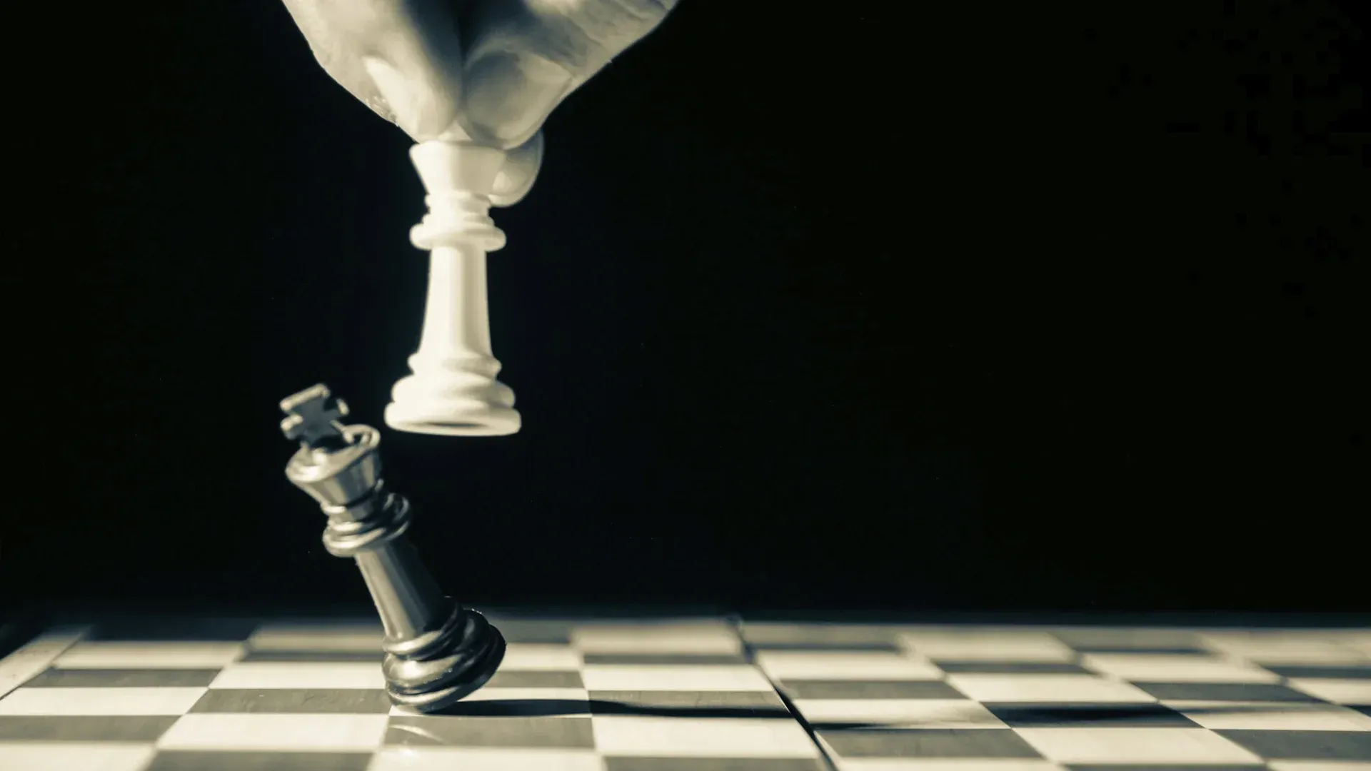 A hand is holding a chess piece over a king on a chessboard.