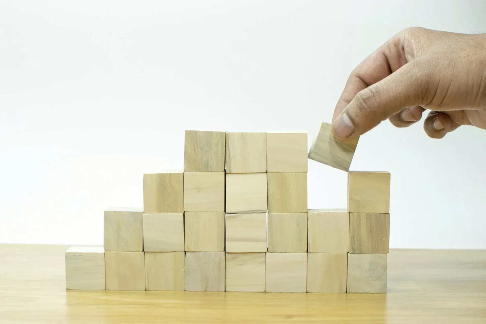 A person is stacking wooden blocks on top of each other on a wooden table.
