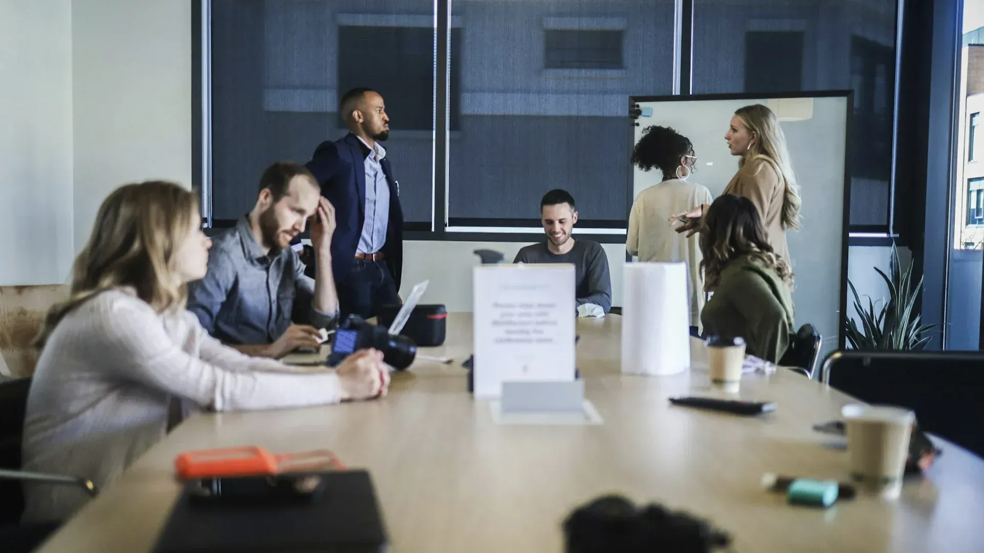 People in a modern office conference room. Some seated, some standing, working on a project.
