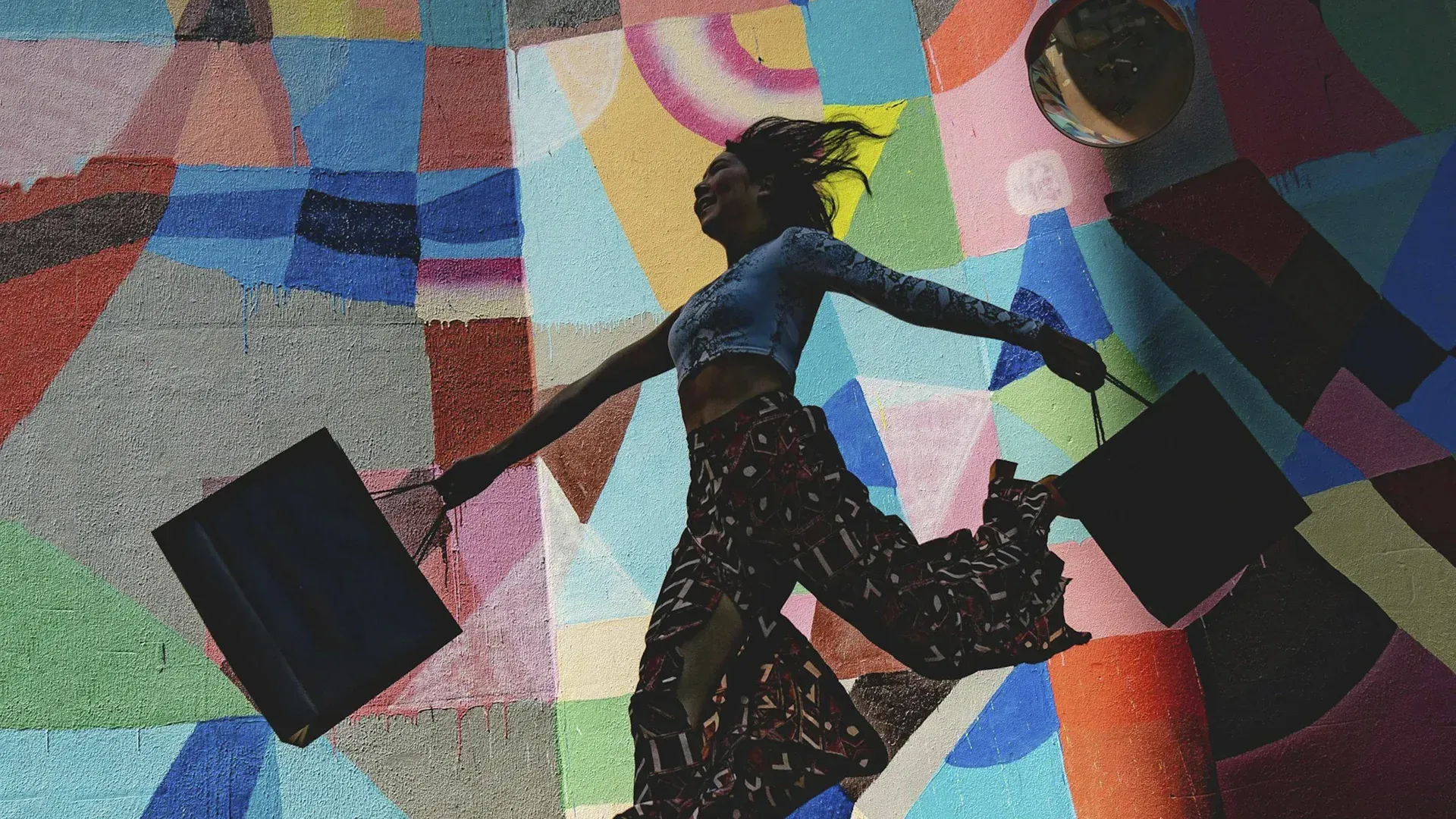 Woman leaping with bags against colorful geometric background.