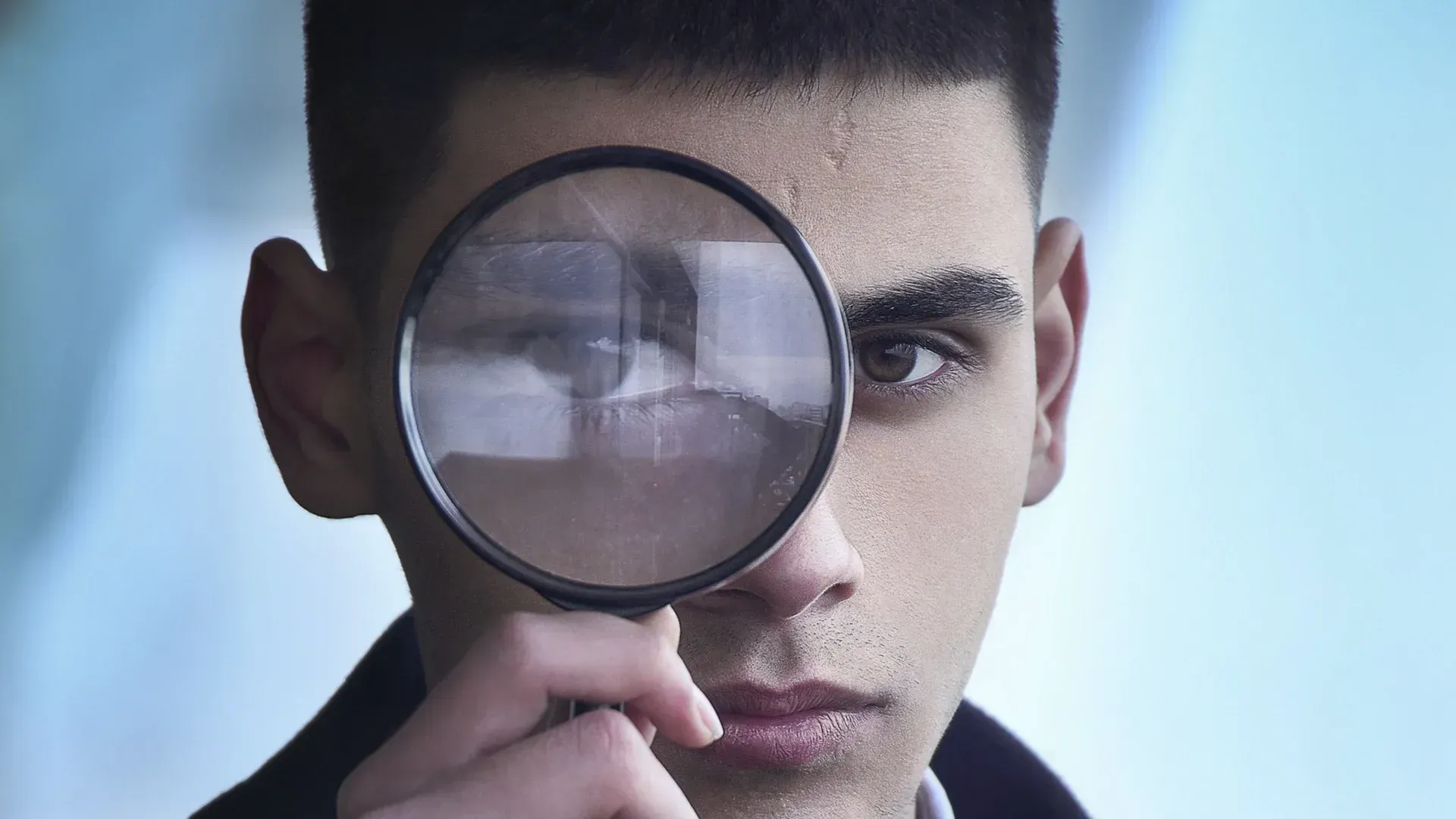 Man looking through a magnifying glass; close up of his eye and face.