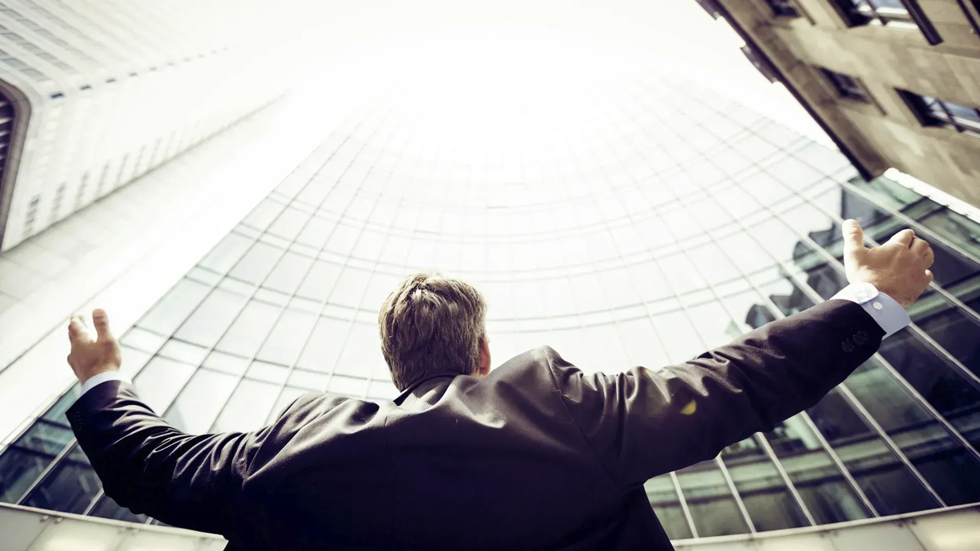 A man in a suit is standing in front of a building with his arms outstretched.
