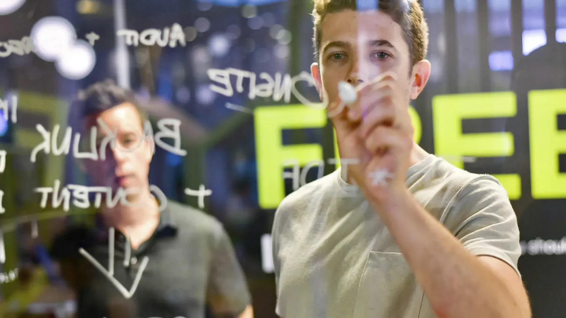 Man writes on glass, another man watches.