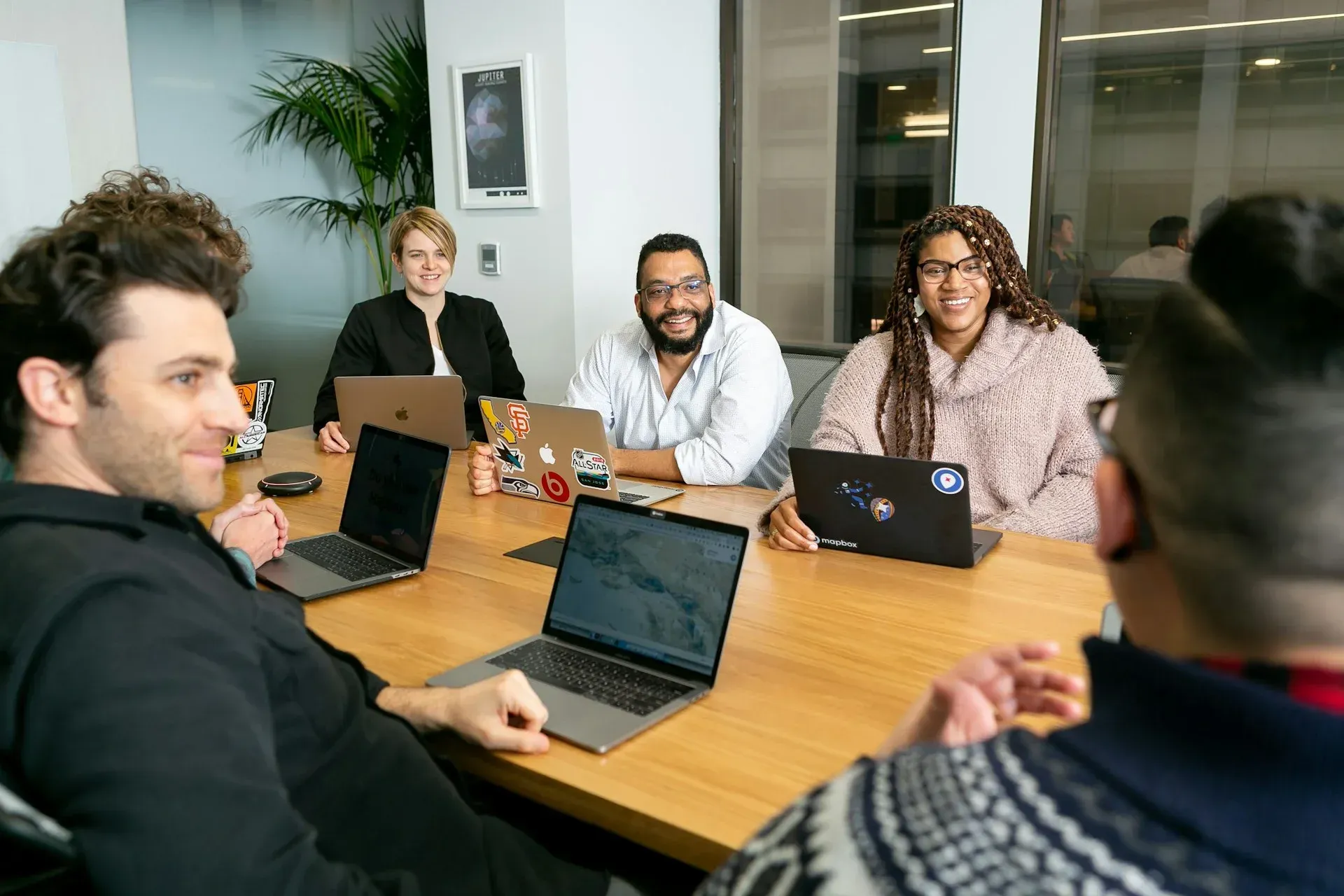 Future Ventures Forum People at a table with laptops in a meeting. Smiling, in an office with a plant.