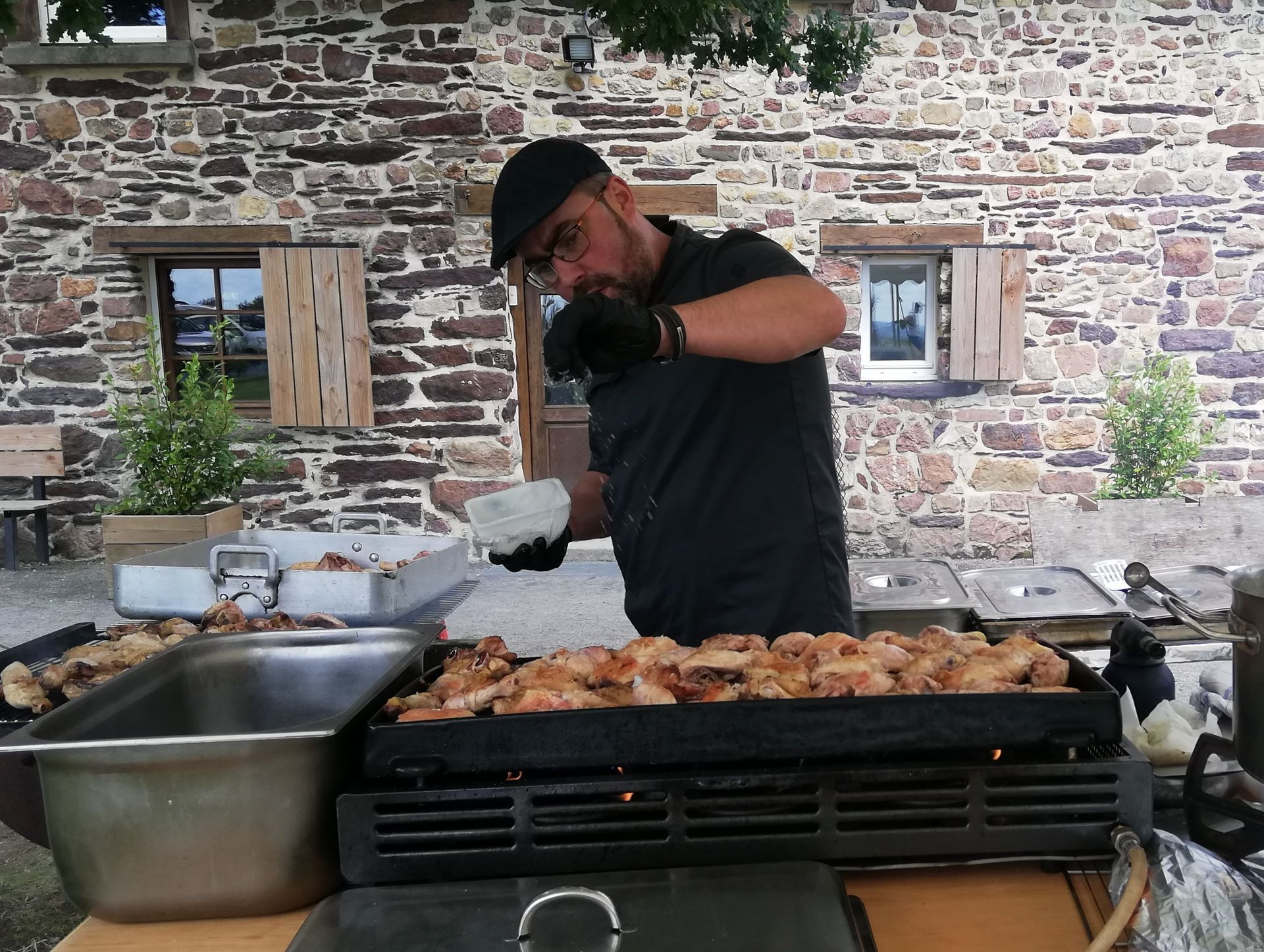 Un homme fait cuire de la nourriture sur un gril devant un bâtiment en pierre.