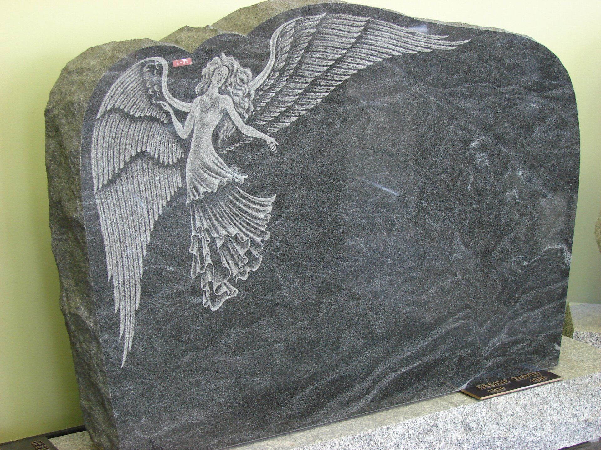 Pierre tombale en granit noir avec un ange sculpté et un espace vierge pour le texte.