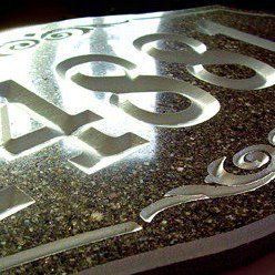 Gros plan sur une plaque de numéro de maison avec des lettres argentées découpées sur un fond de pierre sombre mouchetée.