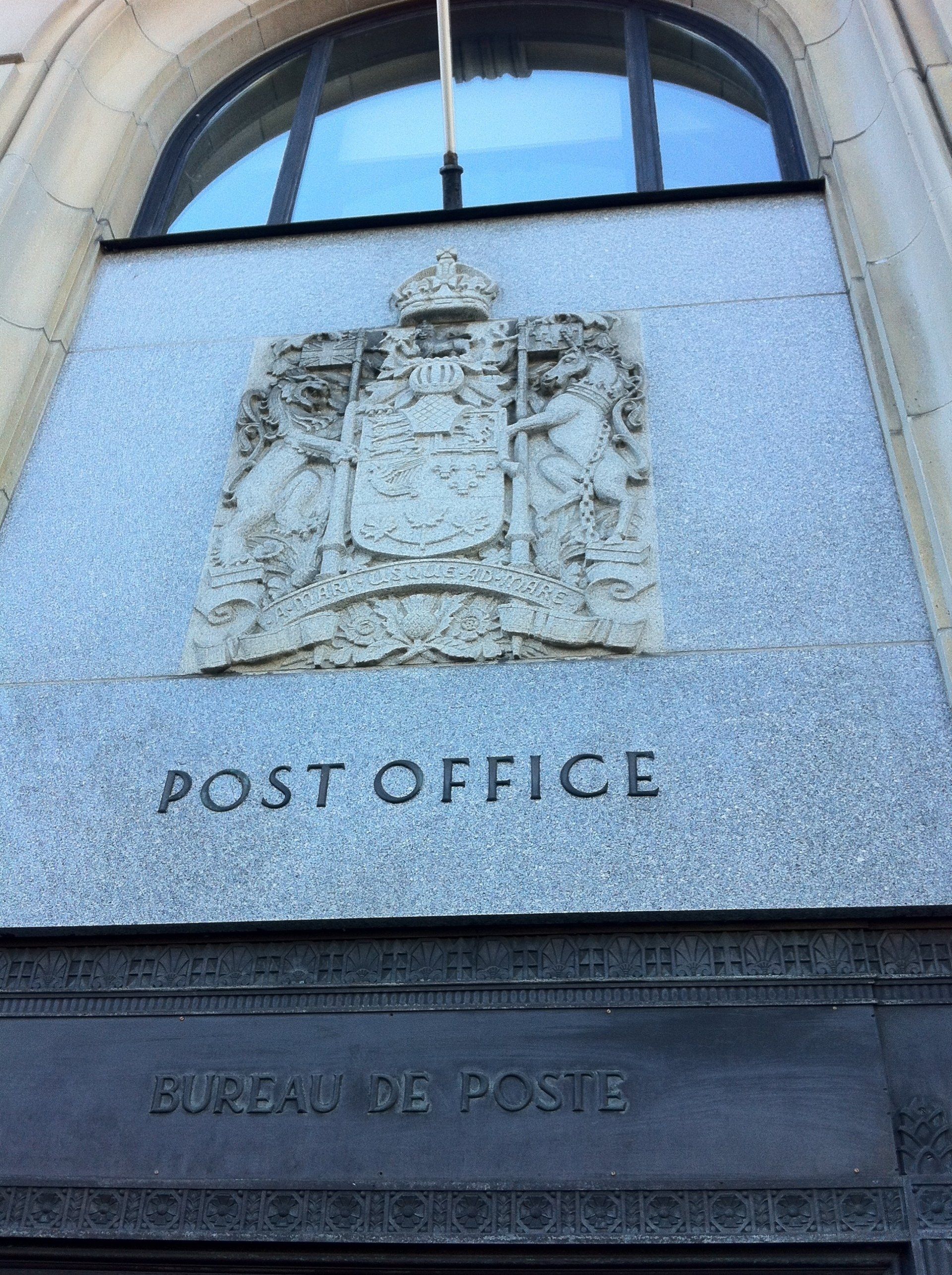 Extérieur d'un bâtiment de poste avec une façade en pierre, un emblème et l'inscription « BUREAU DE POSTE ».