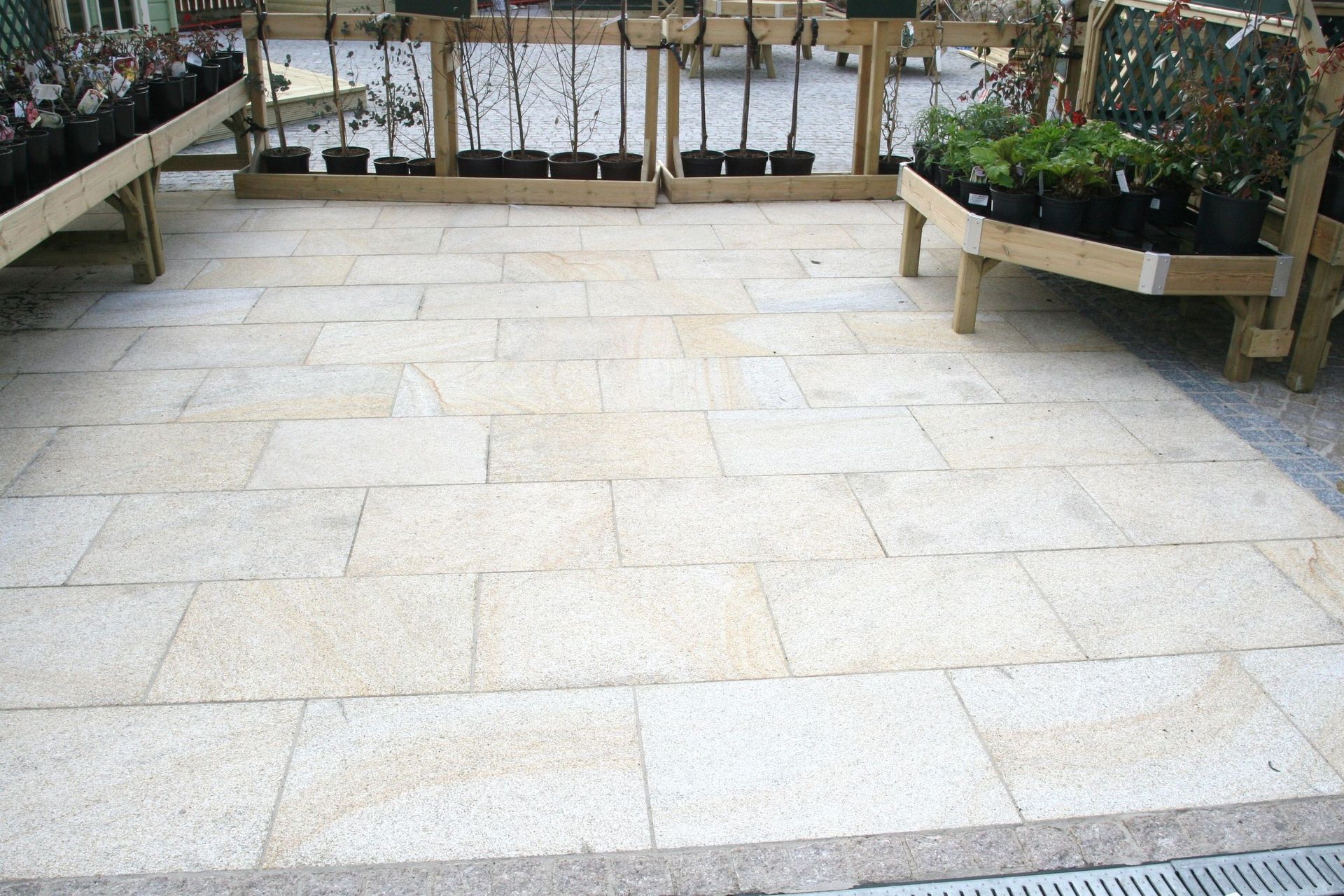 Terrasse en pierre claire avec présentoirs à plantes en bois dans une jardinerie.