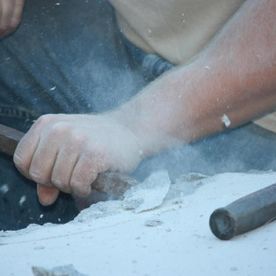 Une personne taille de la pierre, la main agrippant le ciseau, créant de la poussière.