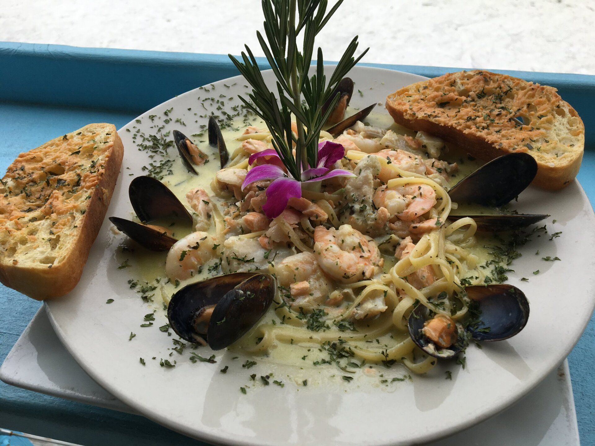 Seafood pasta with mussels, shrimp, and garlic bread, garnished with herbs.