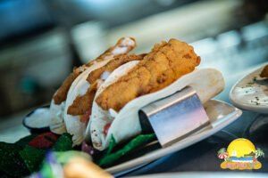 Fish tacos on a plate with fried fish, tortillas, and garnish, possibly in a restaurant.