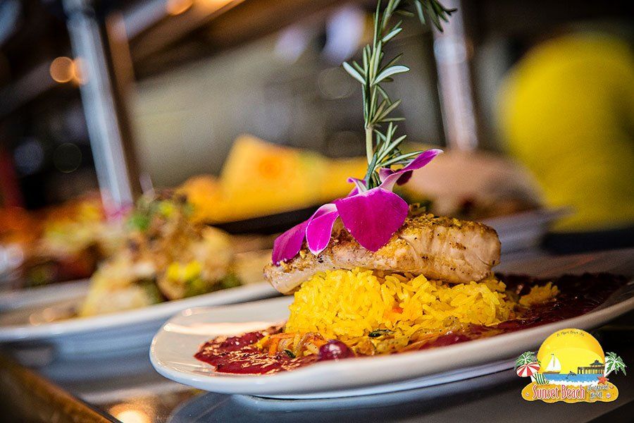 Plate of yellow rice topped with grilled fish, drizzled sauce, garnished with flower and herbs.