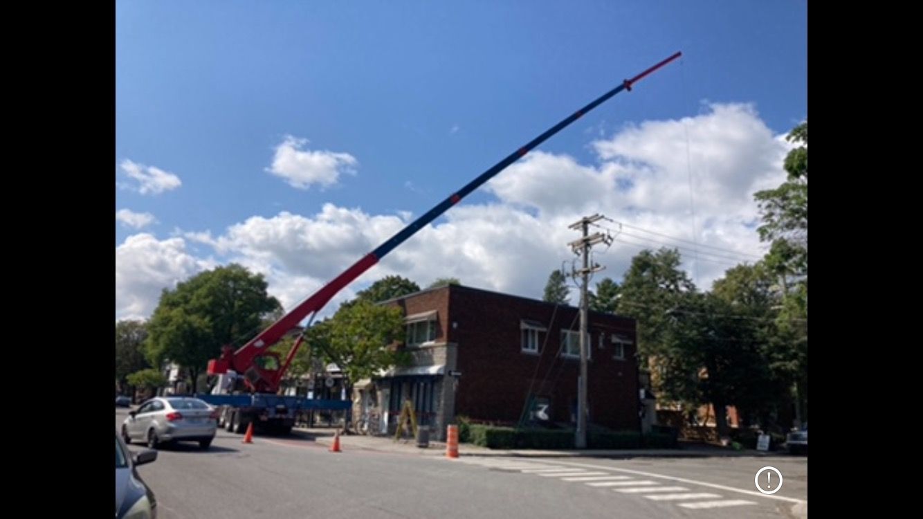 Une grue rouge et bleue est assise sur le bord de la route, devant un immeuble.