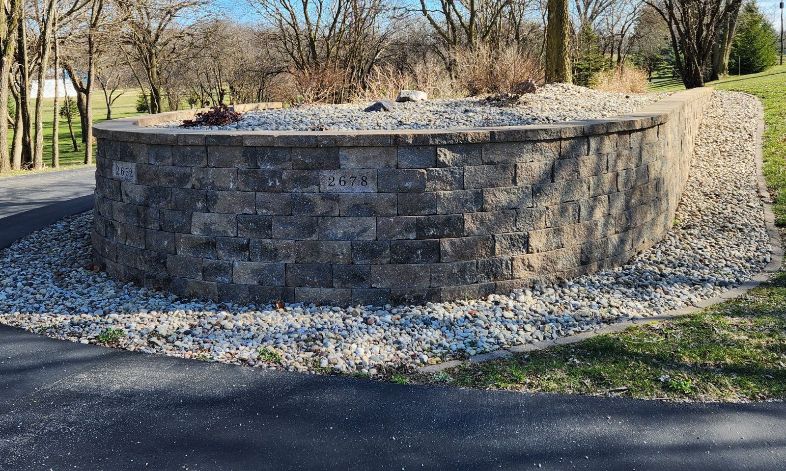 A stone wall is surrounded by gravel and trees on the side of a road.