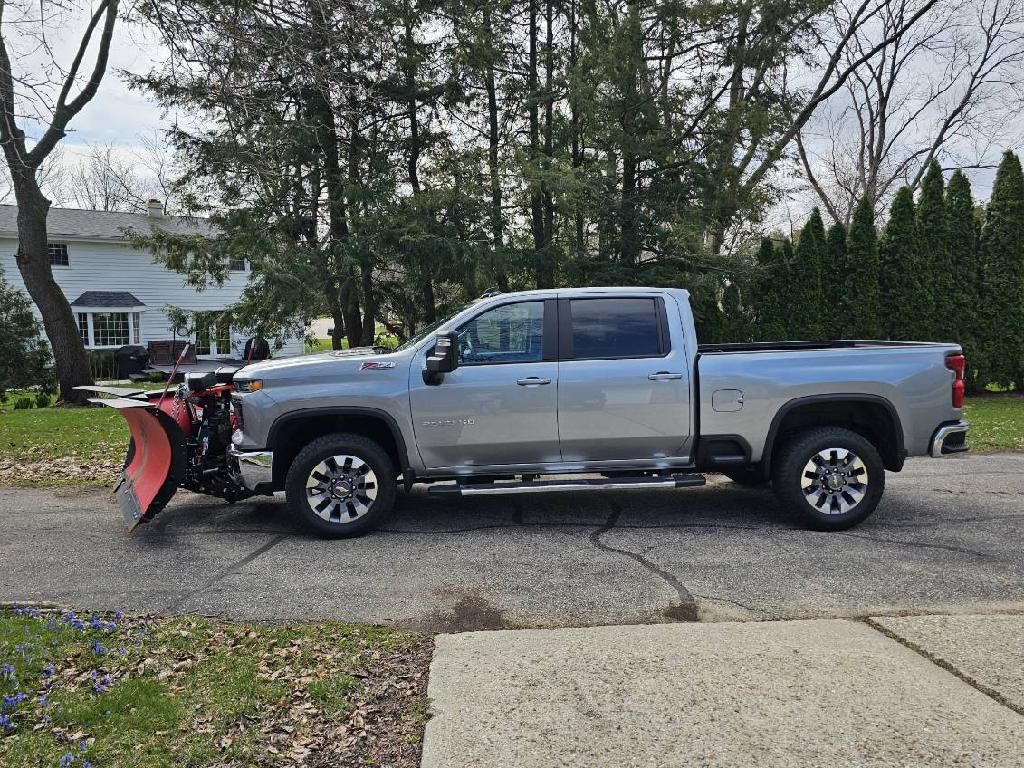 A silver truck with a snow plow attached to it is parked on the side of the road.