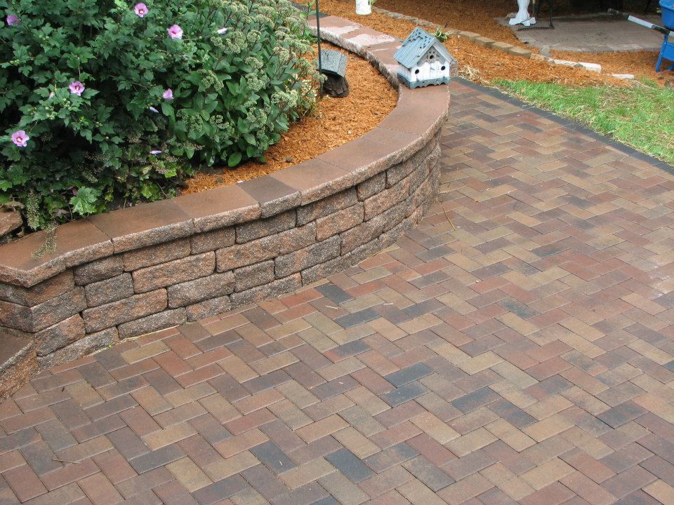 A brick walkway with a brick wall and a birdhouse in the background