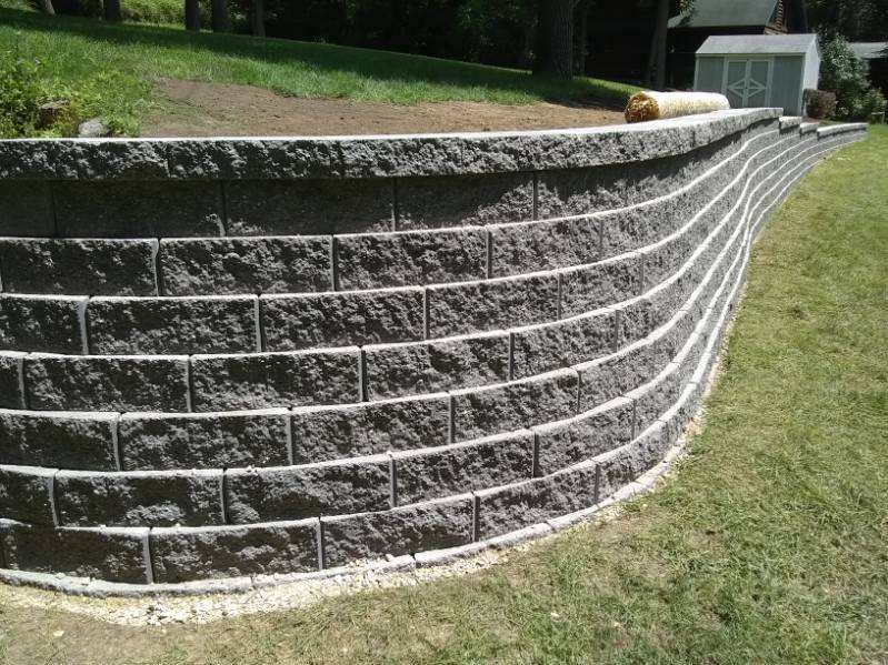 A large brick wall is sitting in the middle of a lush green field.