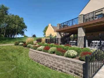 A brick wall surrounds a lush green lawn in front of a house.