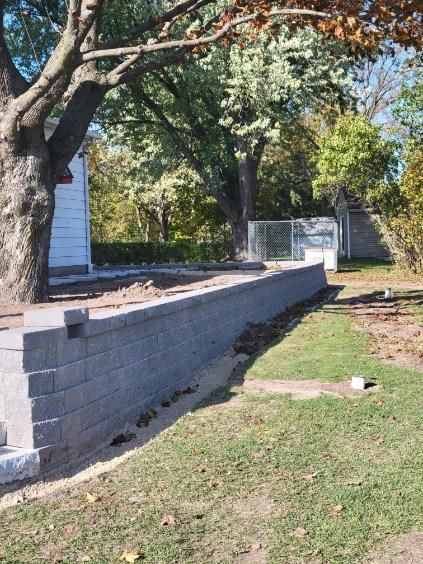 A brick wall is being built in a yard next to a tree.