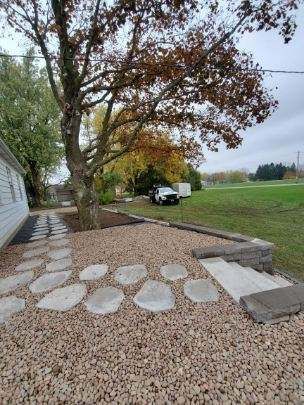 A stone walkway leading to a house with a tree in the background.