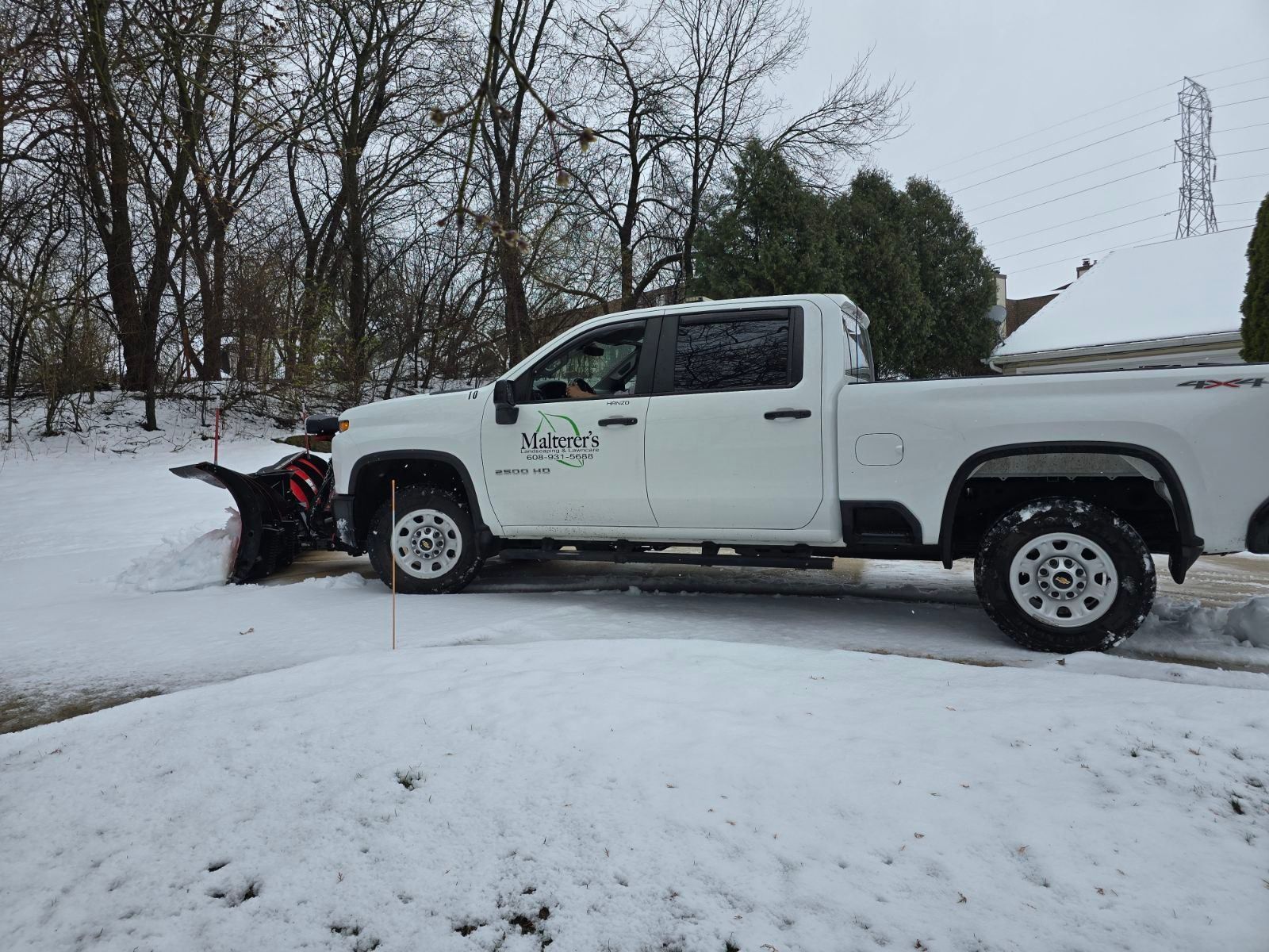 A truck with a snow plow attached to it is parked in front of a house.