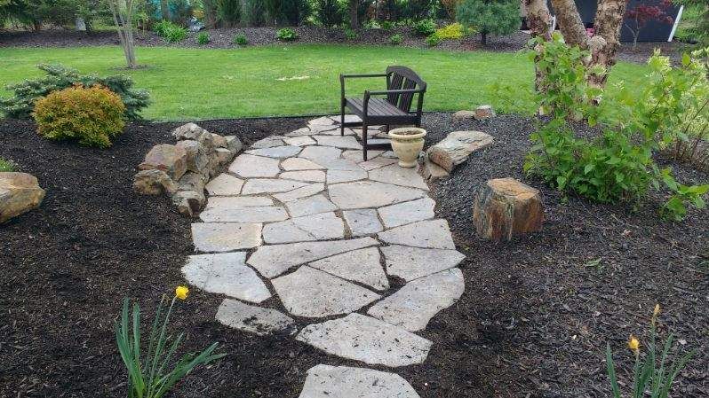 A stone walkway leading to a chair in a garden.