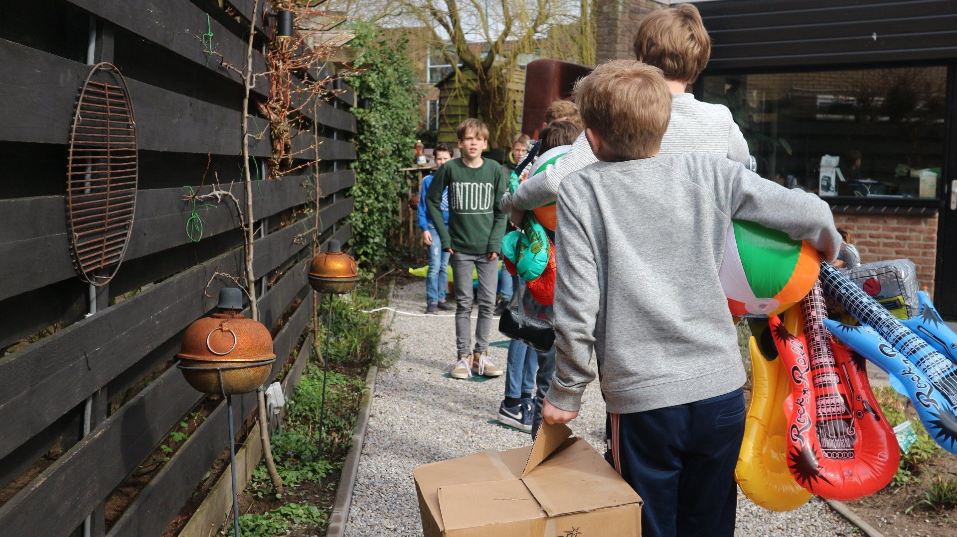 Een groep jonge jongens loopt over het trottoir met een kartonnen doos in de hand.