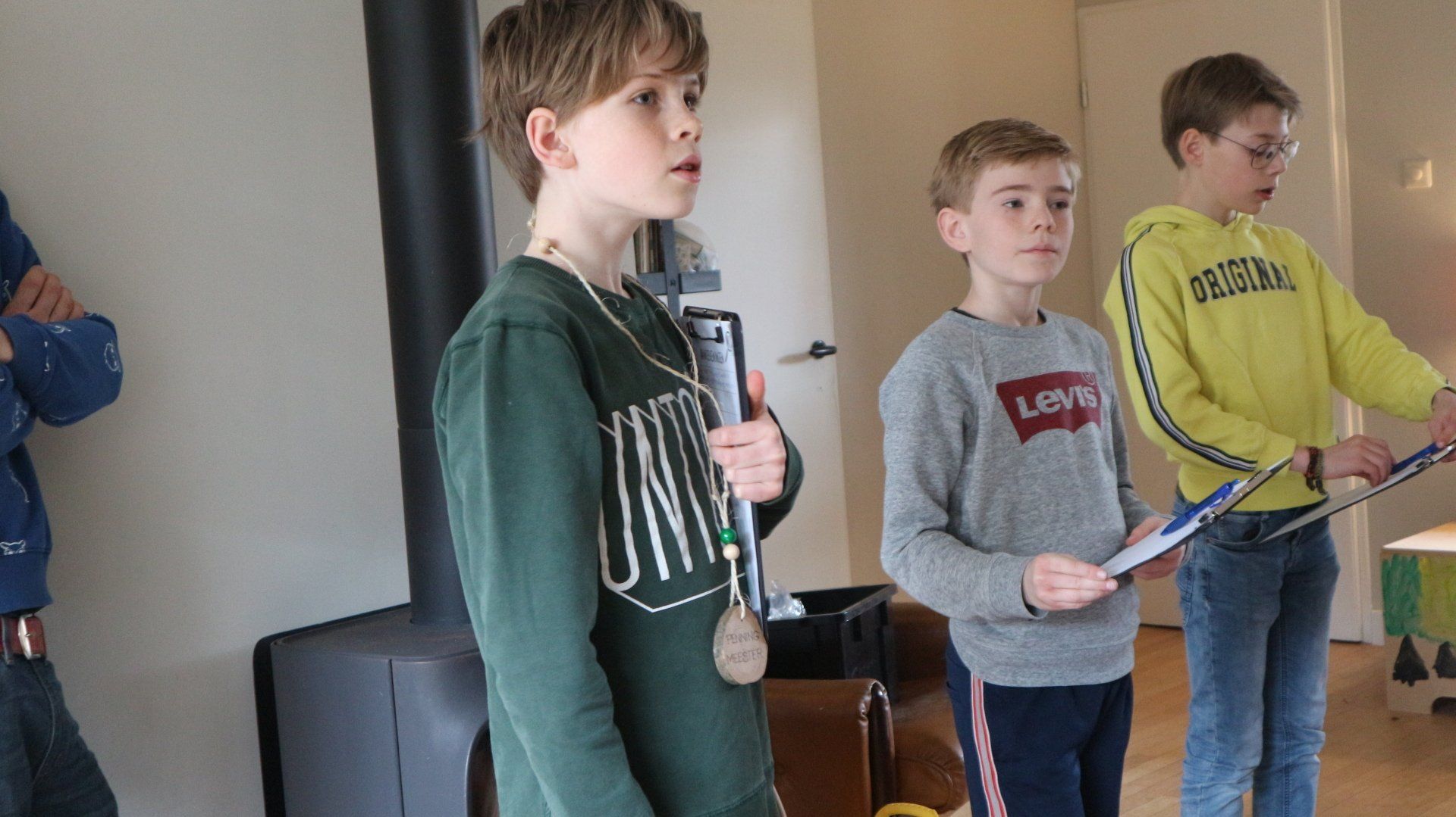 Drie jonge jongens staan ​​in een woonkamer met tennisrackets in hun handen.