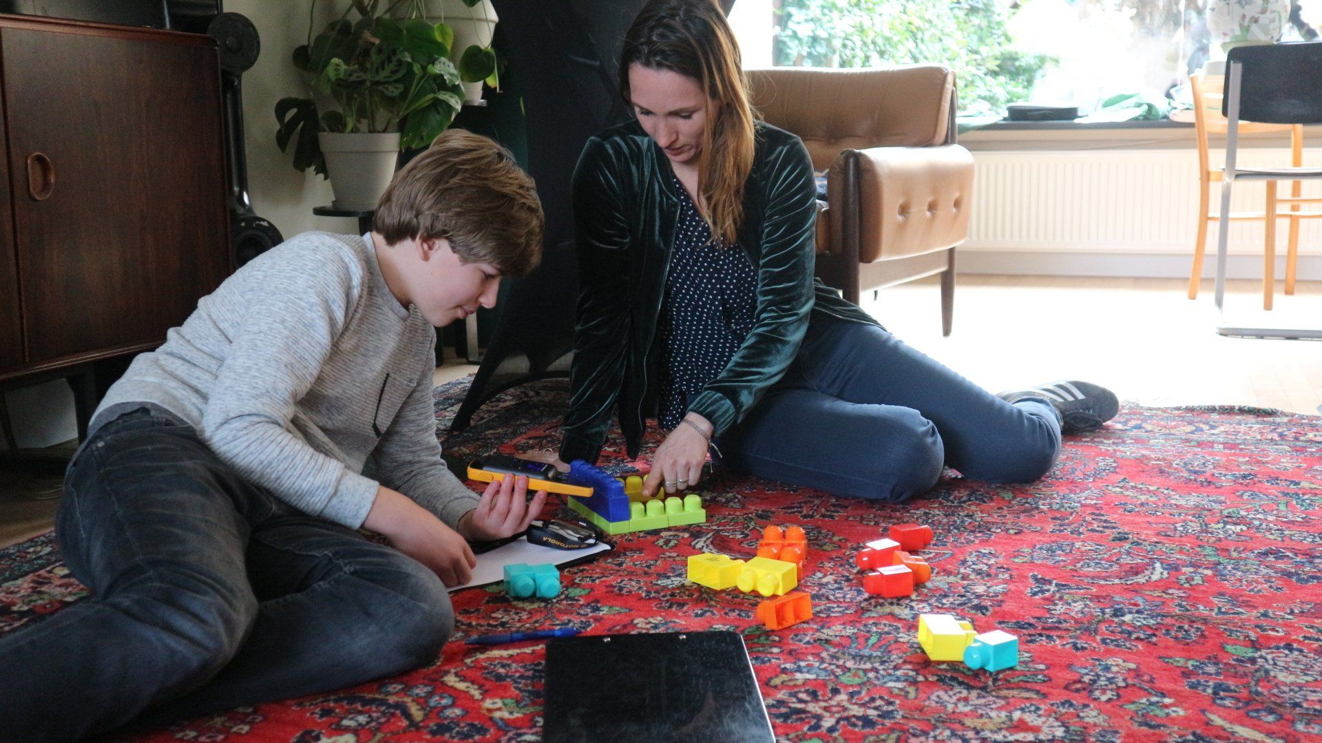 Een vrouw en een jongen zitten op de grond en spelen met speelgoed.
