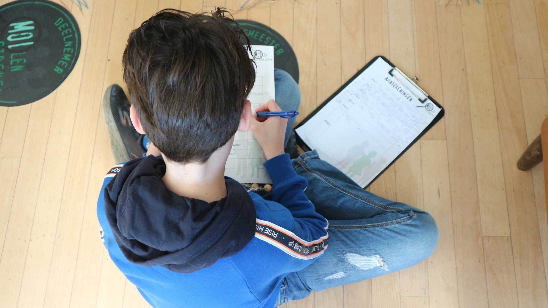 Een jonge jongen zit op de grond en schrijft op een stuk papier.