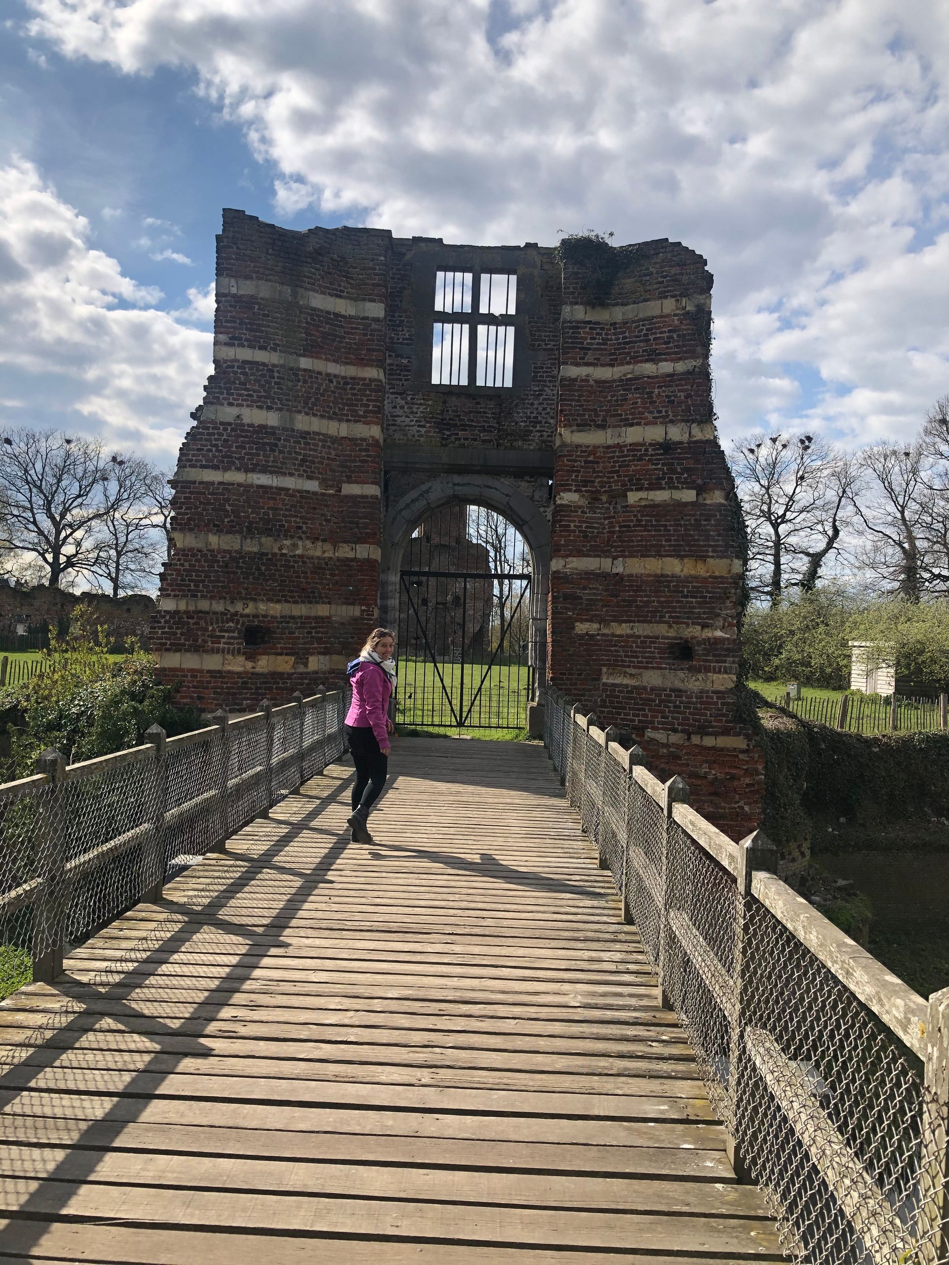 Een vrouw in een roze shirt loopt over een houten brug.