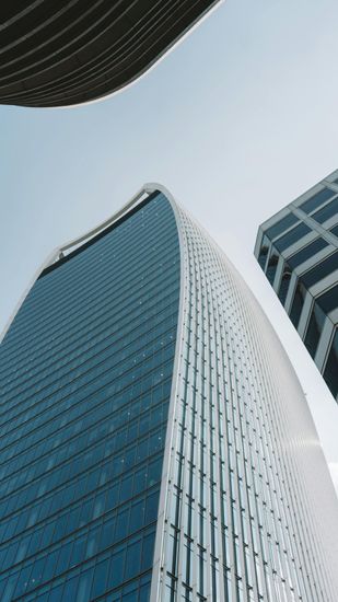 Modern skyscrapers with blue glass facades reaching toward a light blue sky in a city setting.
