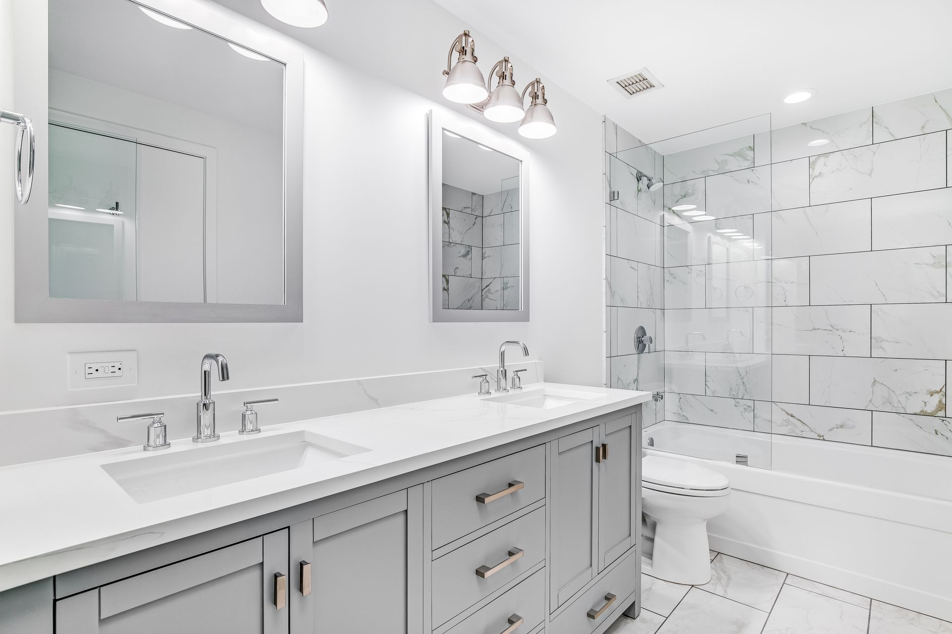 Modern white bathroom with a double vanity, marble-tiled shower, and large mirrors.