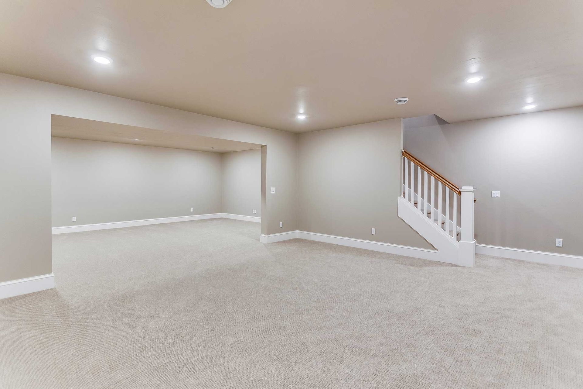 Empty basement room with carpet, stairs, and recessed lighting.
