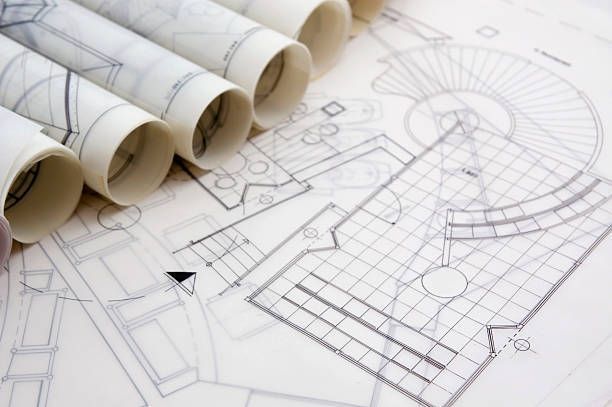 Rolled architectural blueprints and detailed floor plans on a desk, with fine lines and shading.