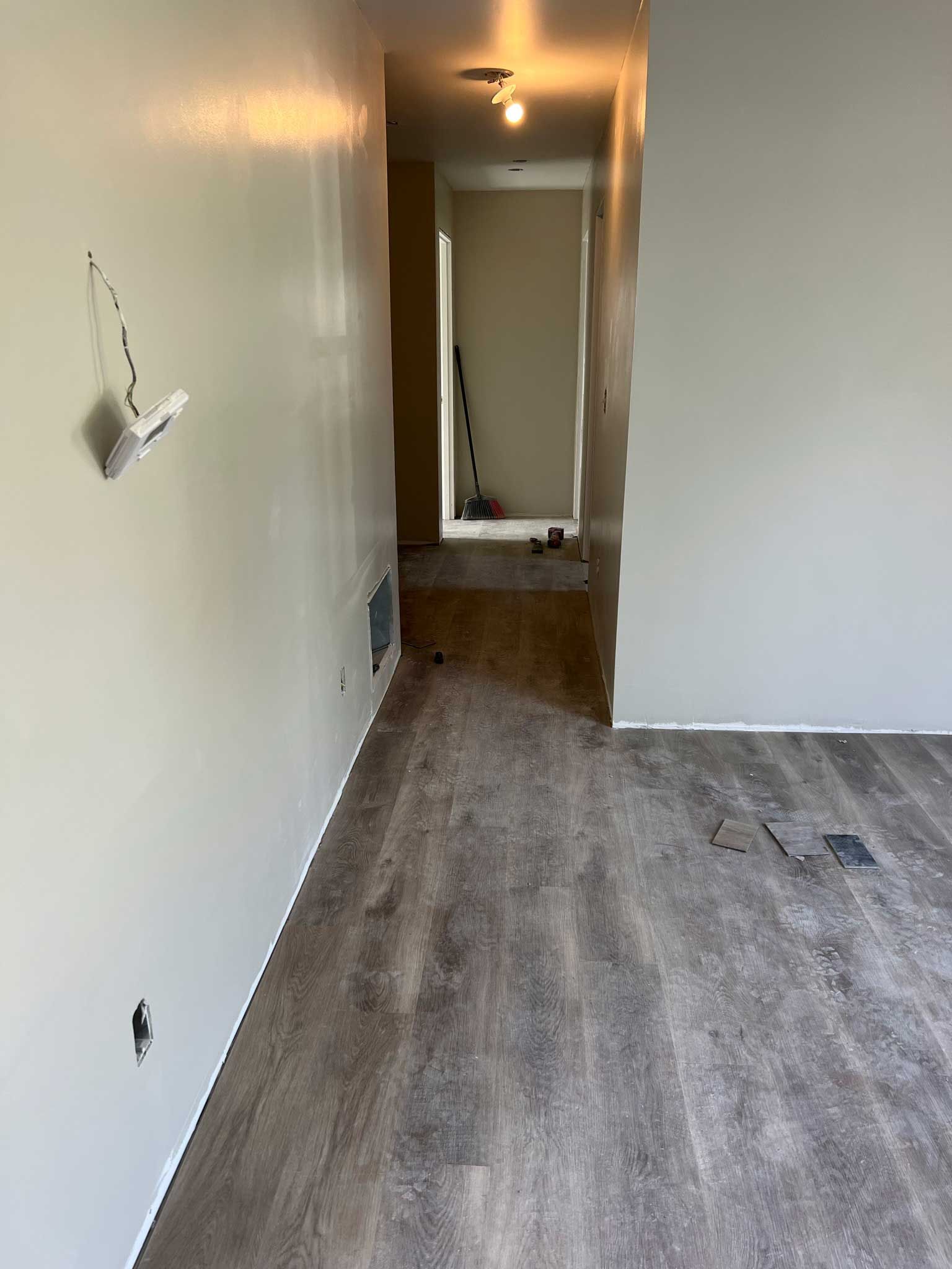 Renovated interior hallway with pale gray walls, new wood-look flooring, and an open doorway.