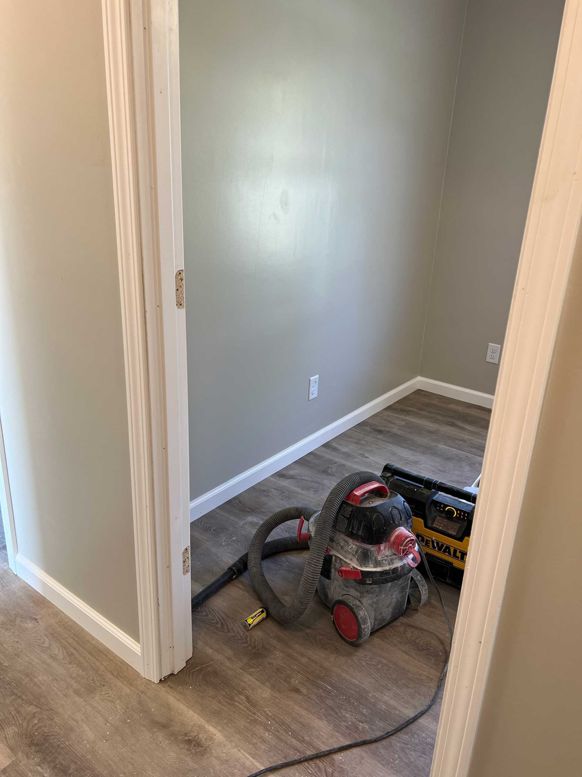 A small, freshly painted room with new flooring. A vacuum cleaner and toolbox rest inside the room.