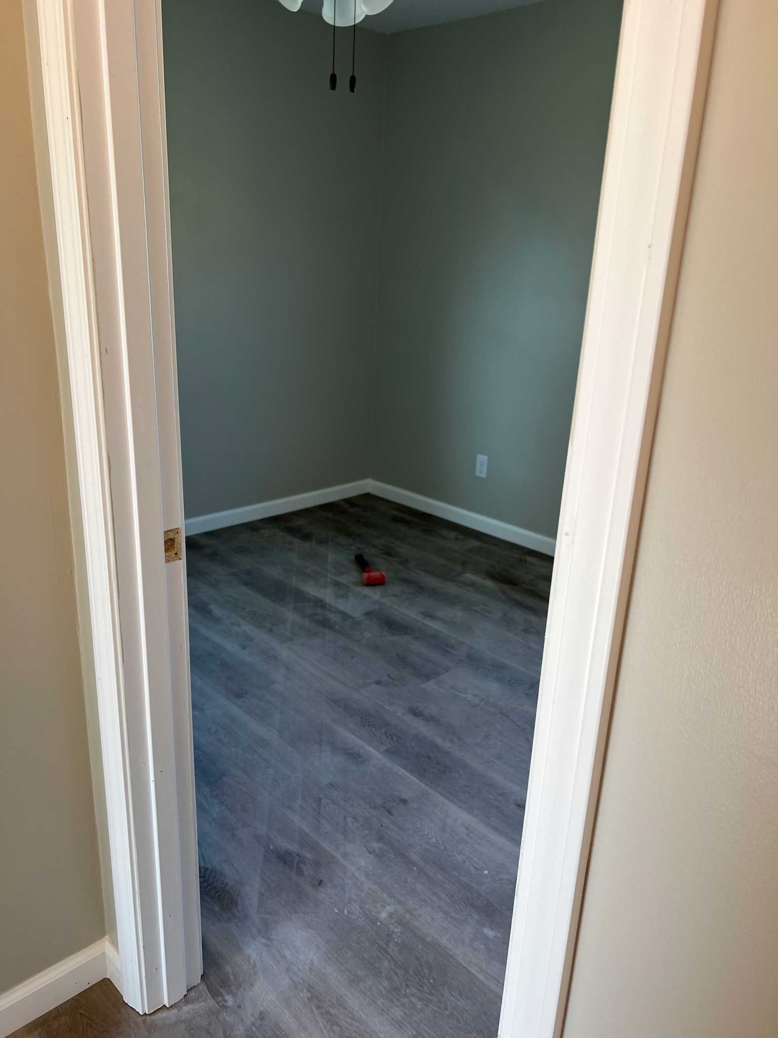 View into a room with gray walls and wood-look flooring through a white door frame.