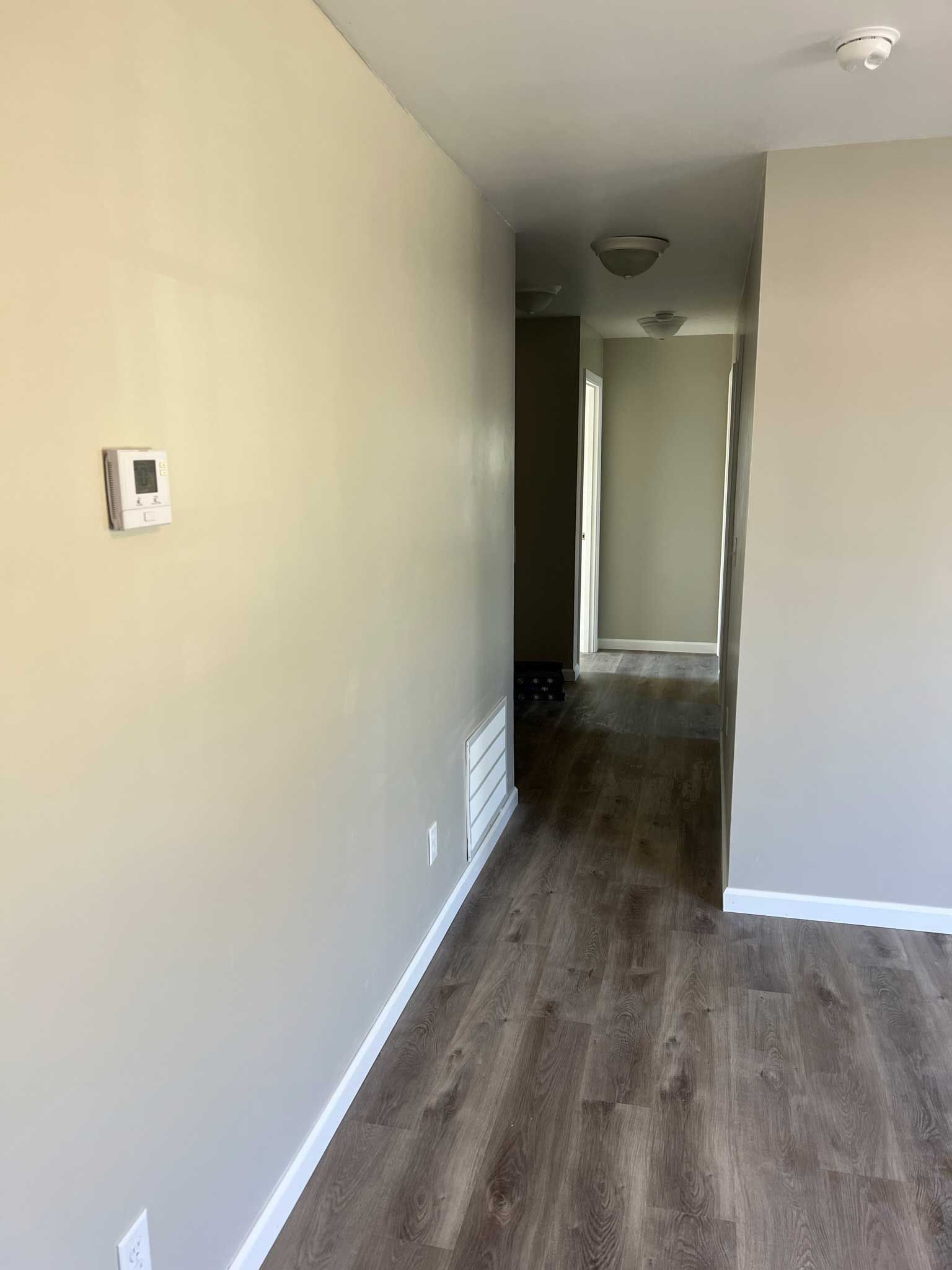 A hallway with light gray walls, laminate flooring, and a thermostat.