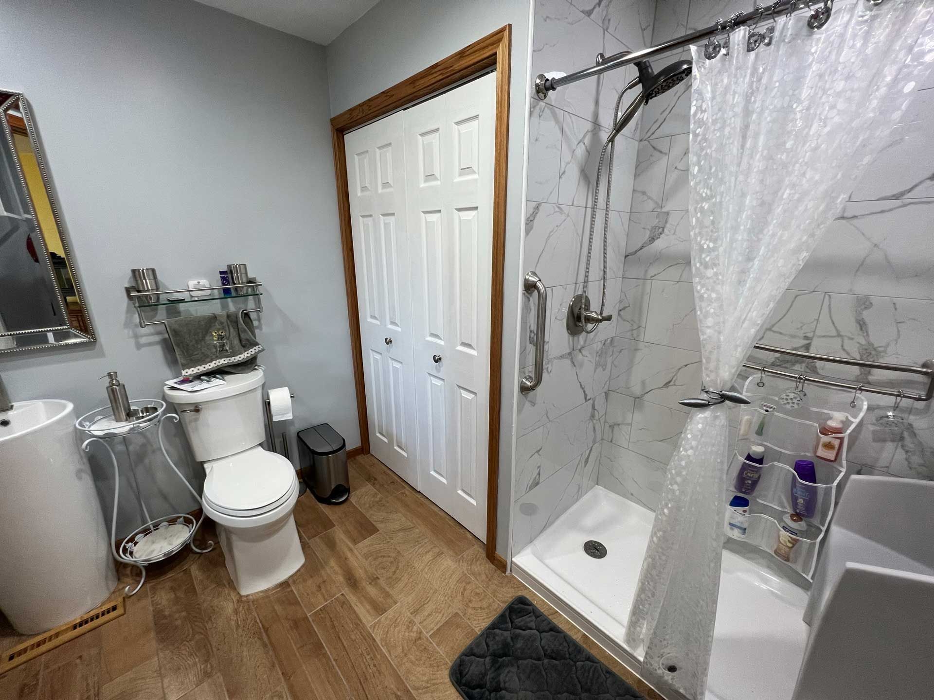 Bathroom with a toilet, pedestal sink, shower with a grab bar, and closed bi-fold door.