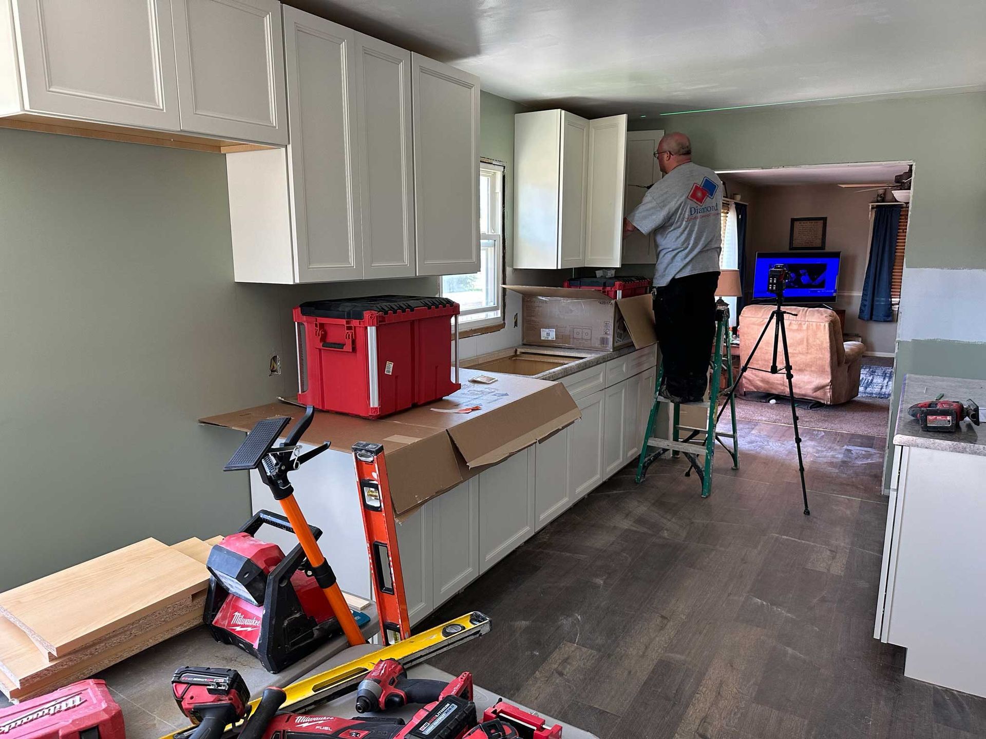Man installing kitchen cabinets; tools and materials are in the room.