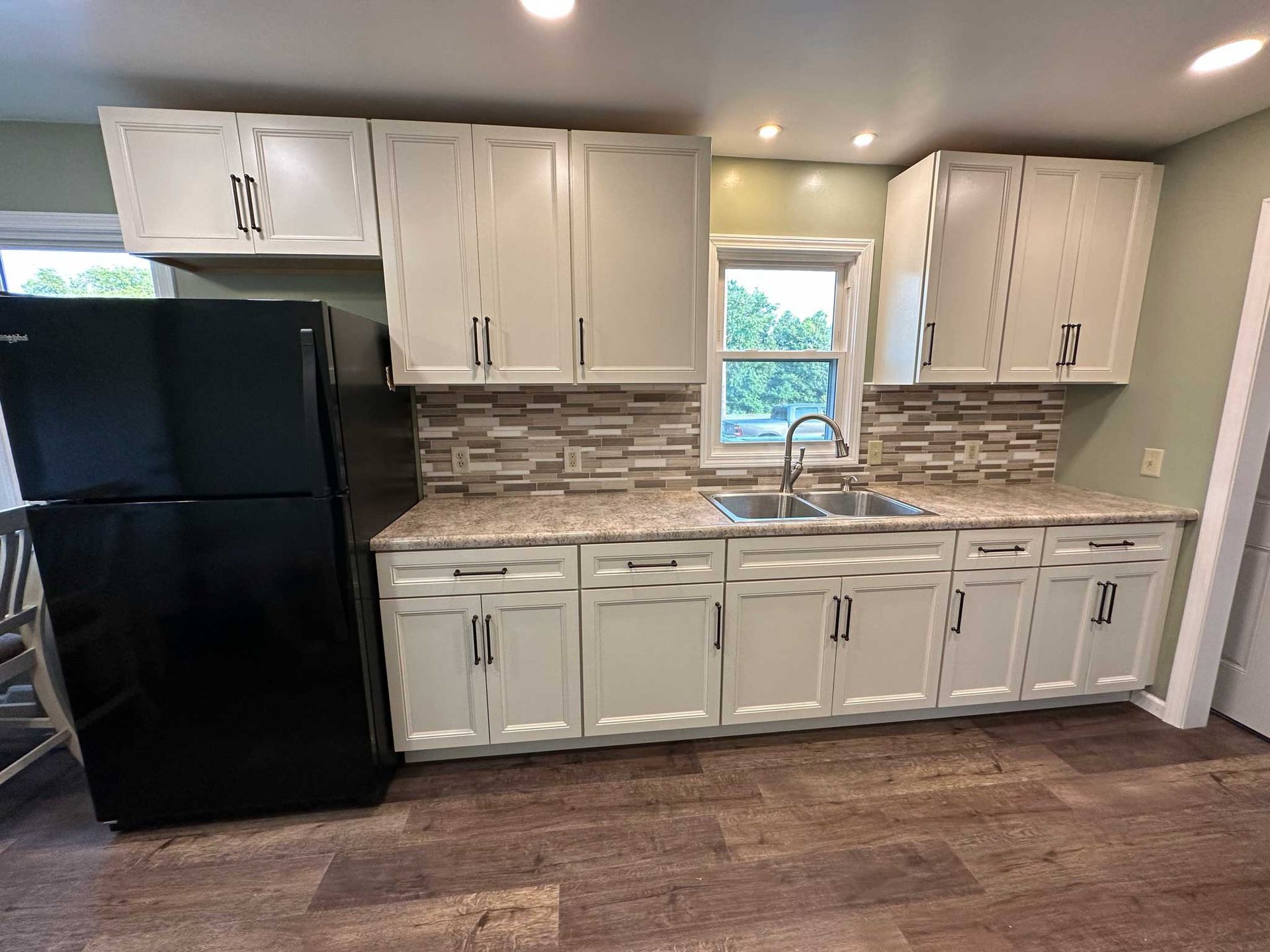 Kitchen with white cabinets, black refrigerator, and wood-look flooring.