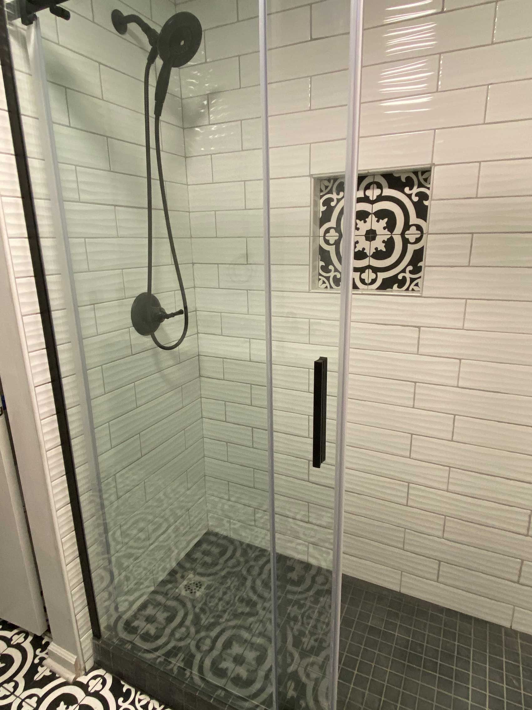 Shower with black fixtures, clear glass door, and patterned tile floor and accent.