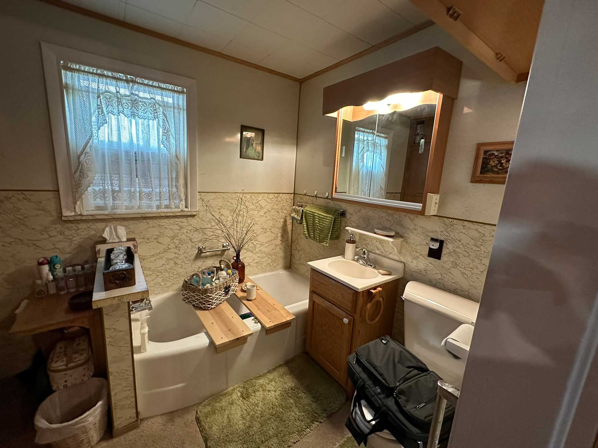 Bathroom with a tub, toilet, vanity, and window. Beige and white tile, wooden accents.