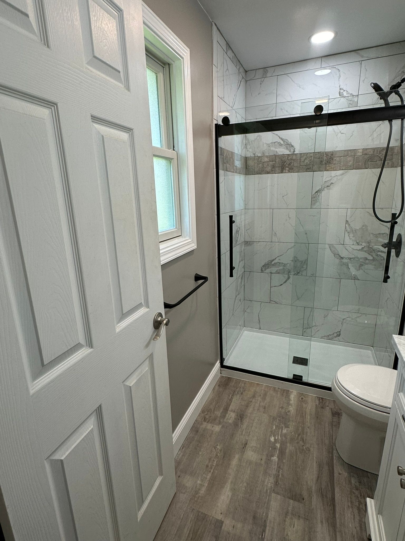 Bathroom with gray vanity, toilet, and white shower, black floor.