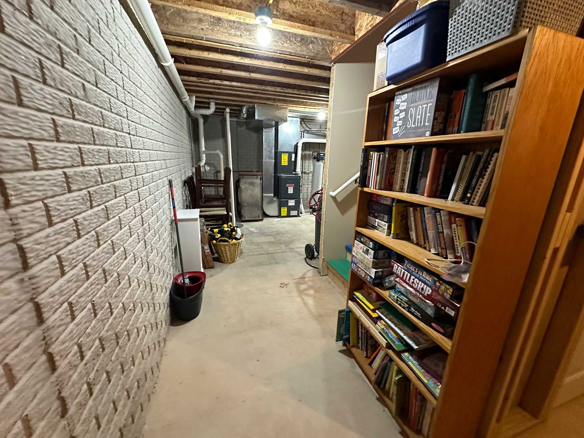 Basement hallway with brick wall, bookshelf, and mechanical equipment.