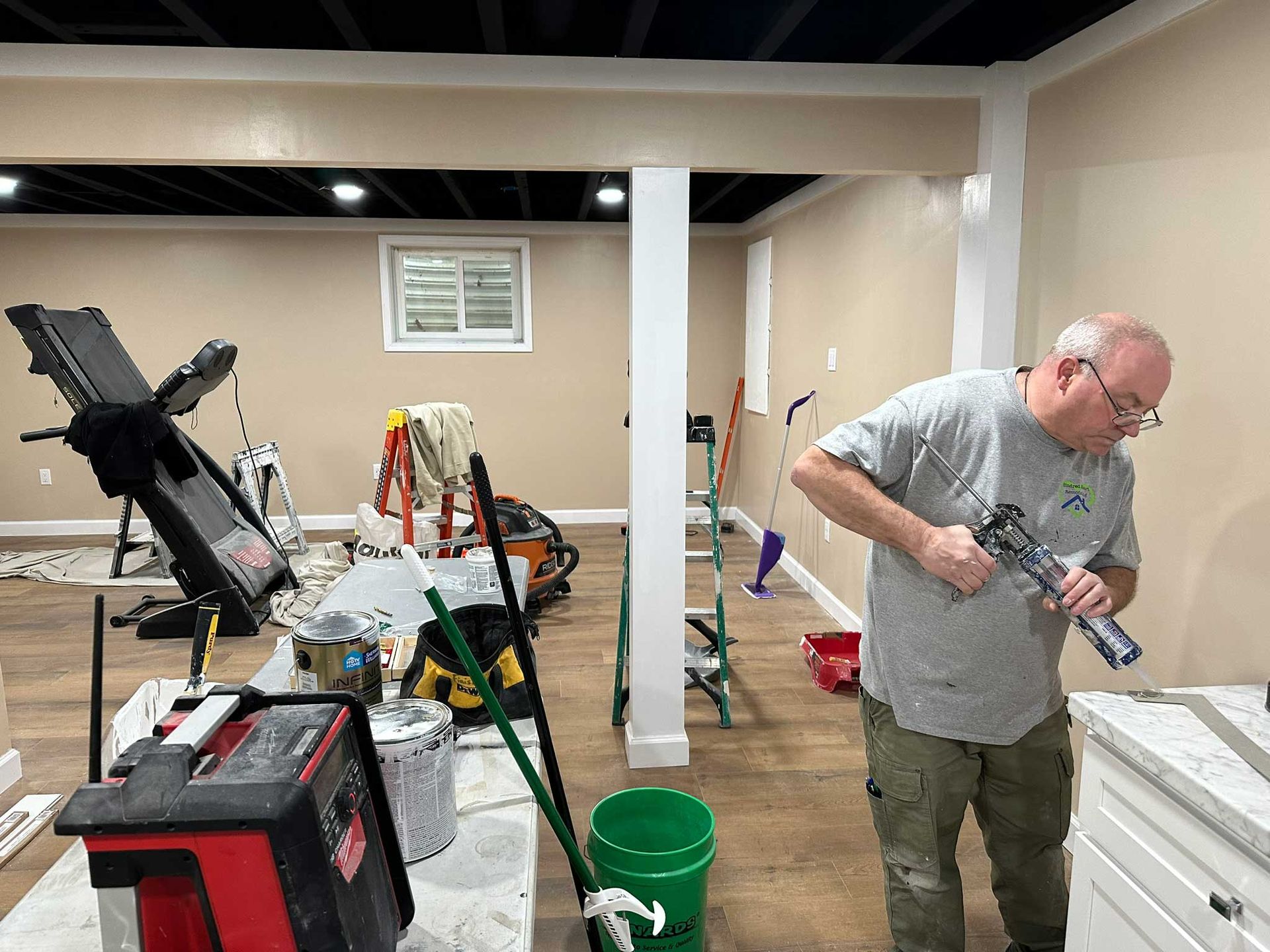 Man in gray shirt working on a project in a room with painting supplies and tools.