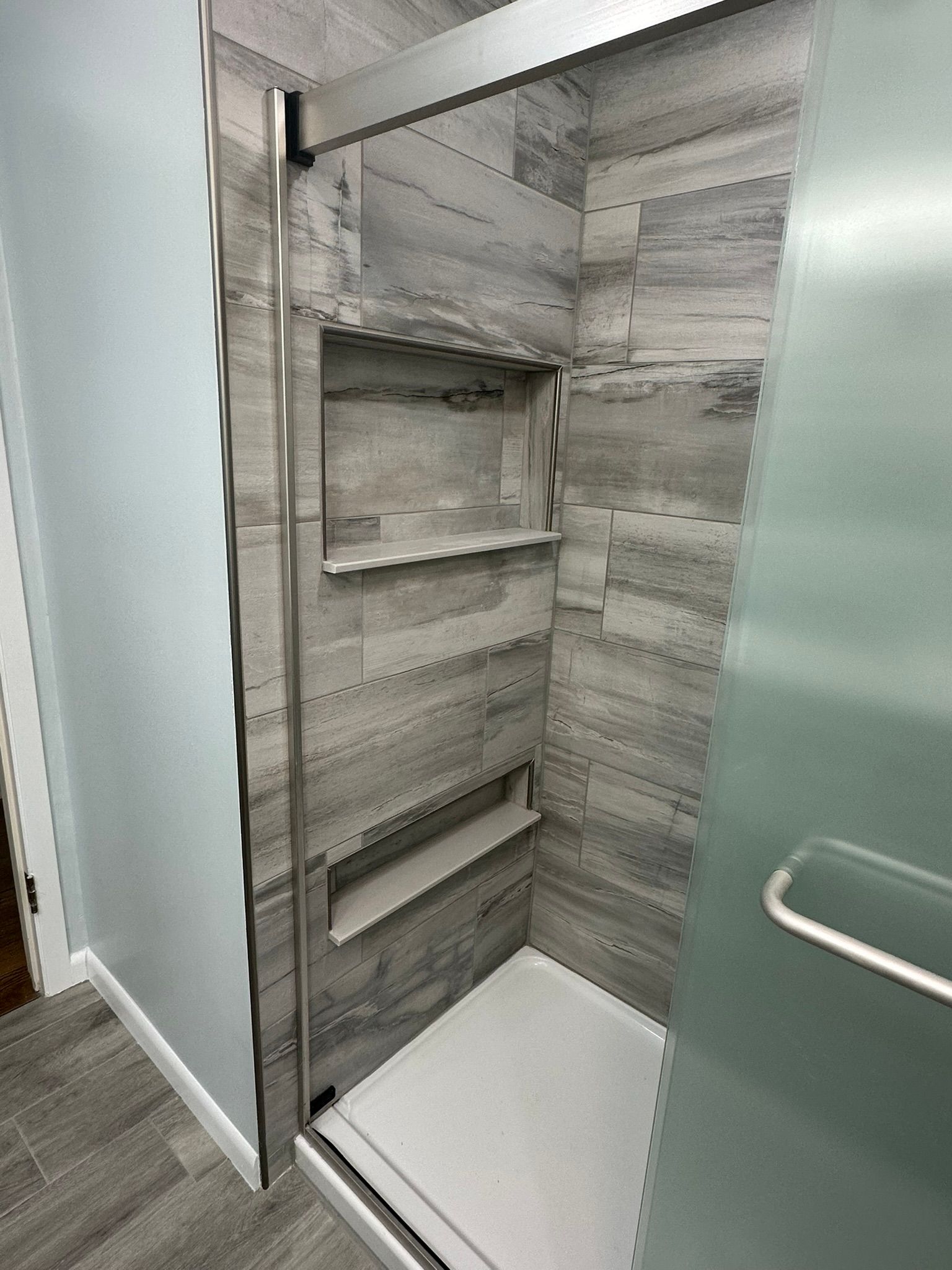 Bathroom with marble shower, white vanity, toilet, and gray tiled floor.